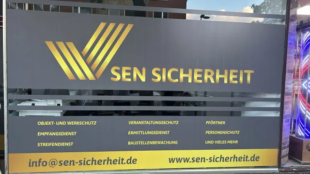 Schaufenster SEN Sicherheit mit goldenem Logo, Leistungsliste und Kontaktdaten auf grauer Folie